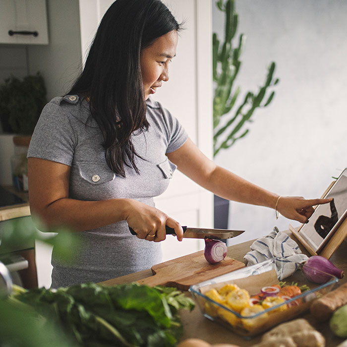 woman slicing vegetables while viewing recipe