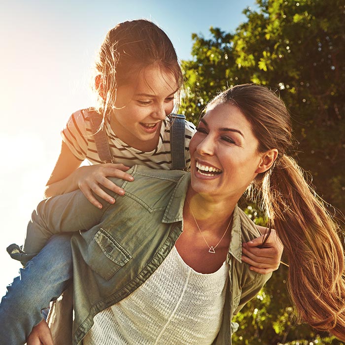 mother smiling with daughter climbing on back