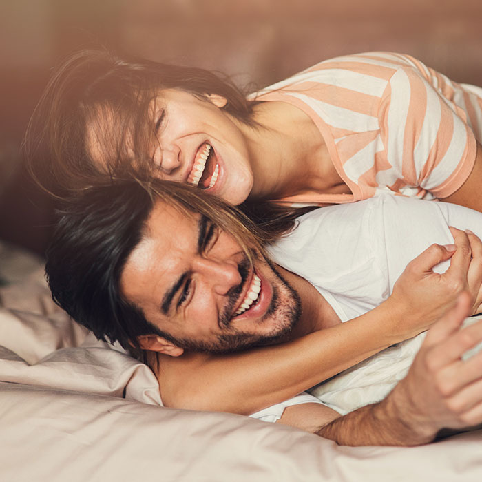 man and woman rolling on bed while laughing