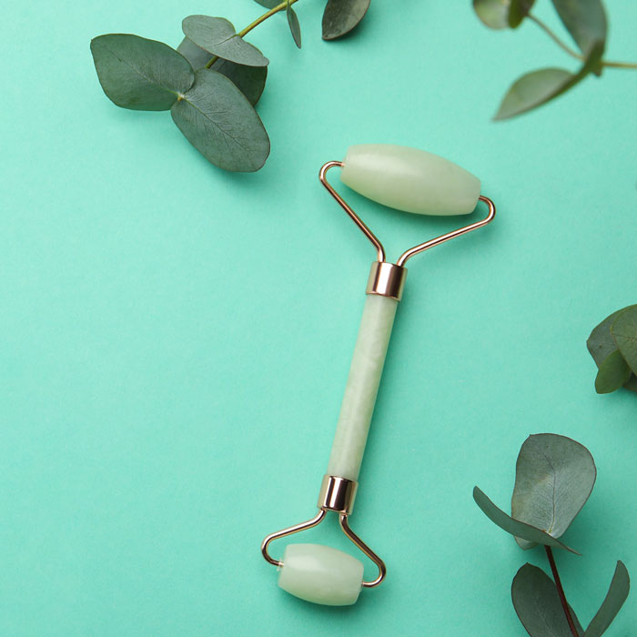 jade facial roller on green backdrop with greenery